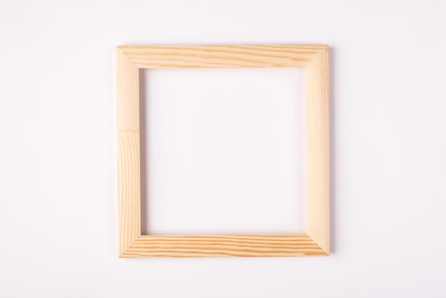 Close up photo of light wooden empty frame hanging on white wall isolated white color background