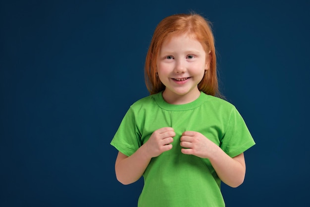 Close up photo of little redhead emotional girl posing before camera on blue background