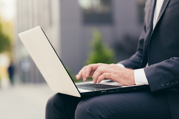 Close-up photo of a male businessman's hand in a business suit working on a white laptop