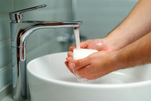 Close up photo of male hands washing with soap above the sink