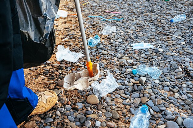 Foto ravvicinata di un uomo che raccoglie immondizia con uno strumento di presa sulla spiaggia