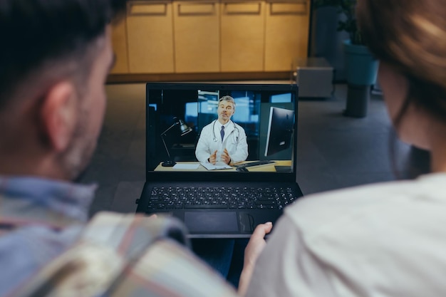 Close up photo of man and woman couple sitting on sofa looking at laptop screen online doctor consultation remotely