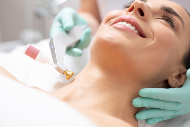 Close up photo of modern cool oxygen lift procedure with a convenient metal tool near the neck of smiling woman