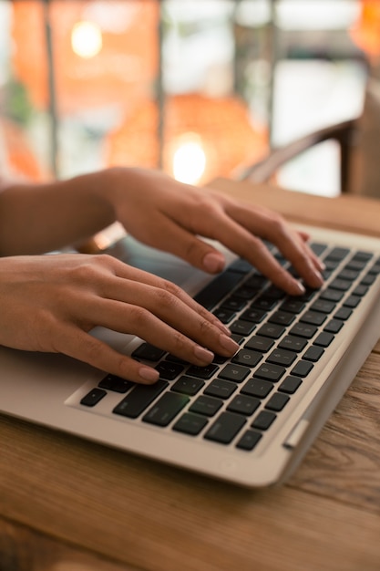 Close up photo of a modern laptop and woman putting both hands on the keyboard while using it