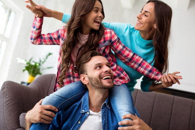 Close up photo of mother, father and their daughter posing together for a joint photo in their stylish living-room, hugging with radiant smiles