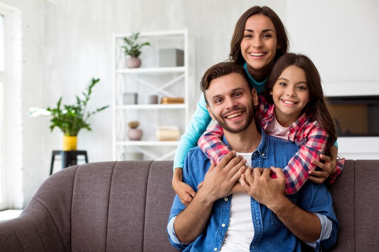Photo close up photo of mother, father and their daughter posing together for a joint photo in their stylish living-room, hugging with radiant smiles