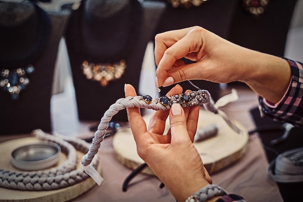 사진 보석 작업장에서 바늘과 실을 사용하여 손으로 목걸이를 만드는 여성의 손 클로즈업 사진.