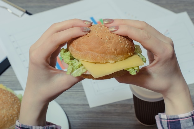 사진 직장에 대한 젊은 노동자의 손에 식욕을 돋우는 햄버거의 사진을 닫습니다