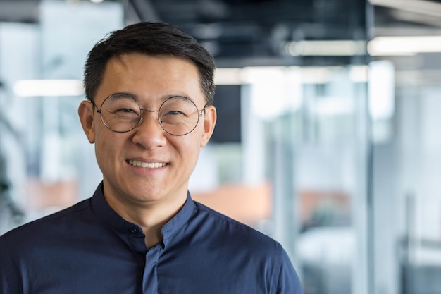 Close up photo portrait of successful young asian investor man in glasses smiling and looking at