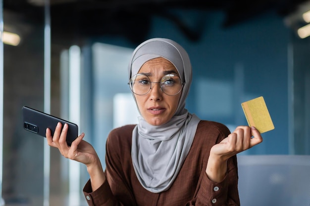 Close up photo portrait of a young arab woman sitting in the office and holding a credit card in her