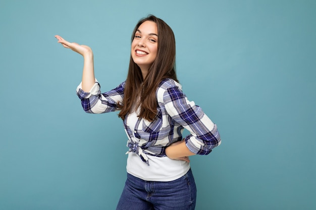 Foto ravvicinata di positivo felice incredibile carino carino affascinante giovane donna che tiene la mano e mostra pubblicità indossando abiti casual isolati su sfondo con spazio di copia.