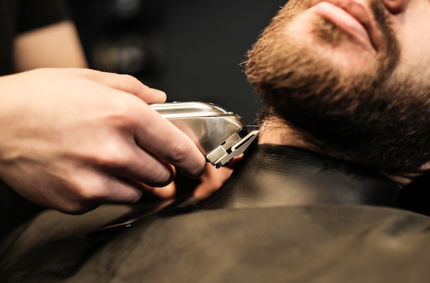 Foto ravvicinata di un parrucchiere professionista, che sta curando la barba del suo giovane cliente, che si guarda allo specchio durante la procedura.