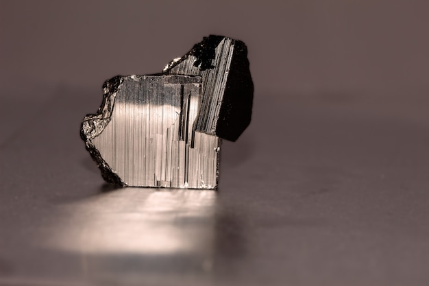 Close up photo of a pyrite mineral on reflective surface. It occurs in cubic, pentagonododecahedral or octahedral crystals, sometimes with alternating faces striated longitudinally