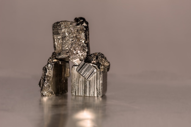 Close up photo of a pyrite mineral on reflective surface. It occurs in cubic, pentagonododecahedral or octahedral crystals, sometimes with alternating faces striated longitudinally