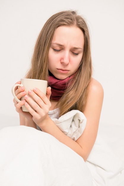 Chiuda sulla foto della ragazza malata che tiene una tazza di tè caldo