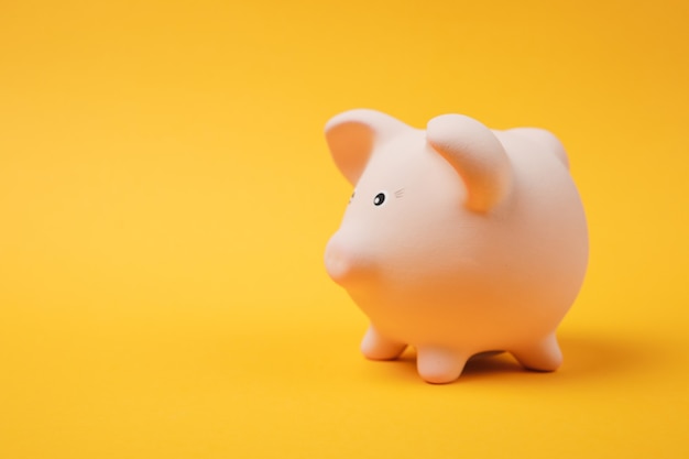 Close up photo, side view of pink piggy money bank isolated on bright yellow wall background. Money accumulation investment banking or business services wealth concept. Copy space advertising mock up.