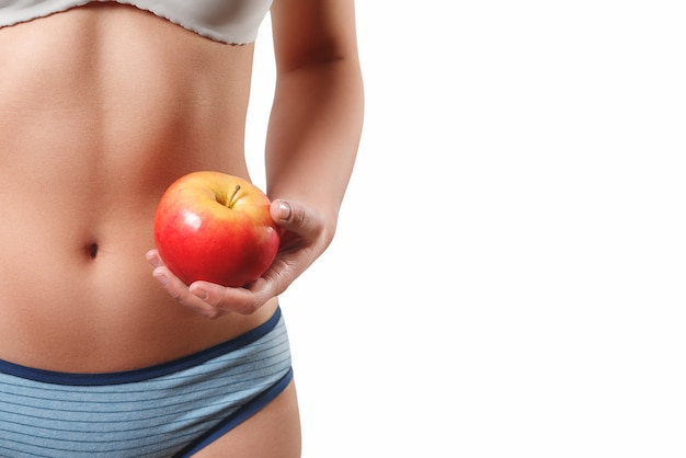 クローズアップ写真細身スリムな体型ウエスト腹若い女性の女の子白い背景で隔離のジューシーな赤いリンゴを保持