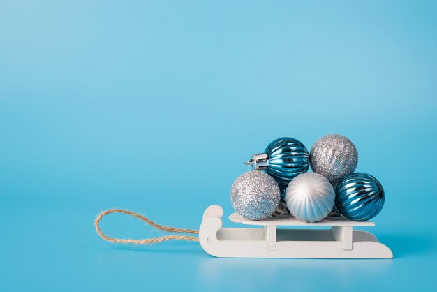Foto ravvicinata di piccole slitte che trasportano un mucchio di affascinanti giocattoli lucenti alla moda isolati su uno sfondo di colore blu con uno spazio vuoto