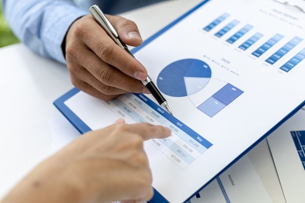 Photo close-up photo of two businessmen pointing at a sales data sheet in graph format, they are meeting together on the topic of managing sales growth. concept of business cooperation and sales management.