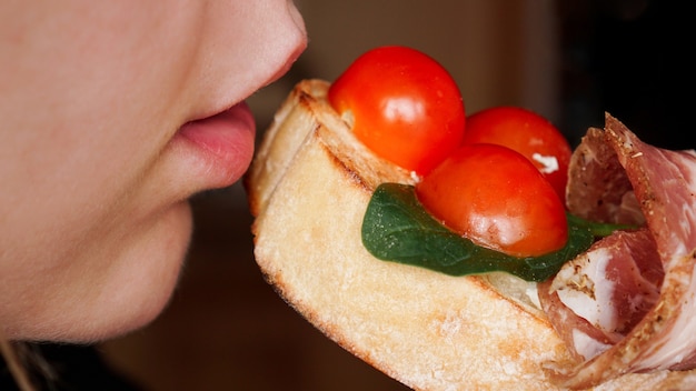 Foto foto in primo piano. la donna morde la bruschetta fresca con il pomodoro ciliegia. antipasto italiano delizioso.
