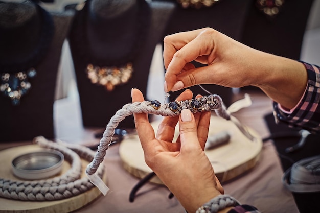 Close-up photo of a woman's hands who makes handmade necklaces, working with needles and thread in jewelry workshop.