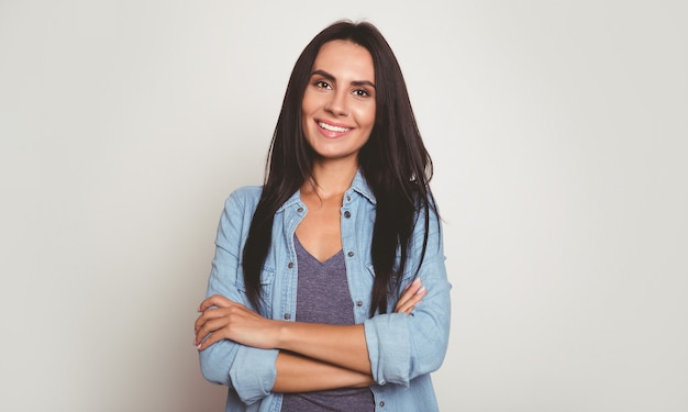 Close-up photo of a young and beautiful girl in casual outfit, who is posing with folded arms, looking in the camera and smiling broadly