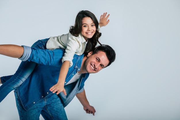 Close-up photo of a young dad and his little child, who are hugging tenderly and smiling, while looking in the camera together.