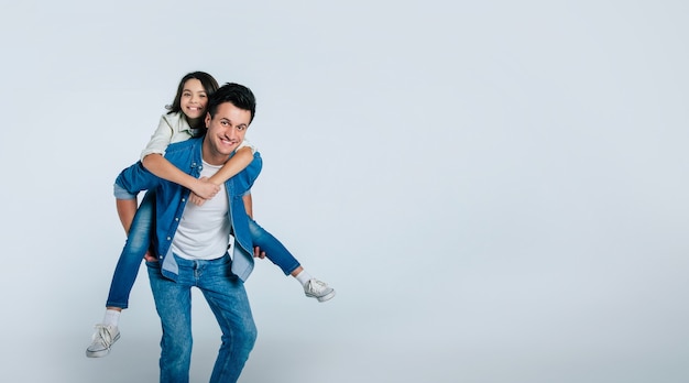 Close-up photo of a young dad and his little child, who are hugging tenderly and smiling, while looking in the camera together.