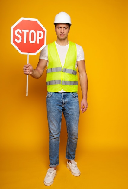 Close up photo of young happy and confident foreman or architect in build helmet is posing isolated on yellow background.