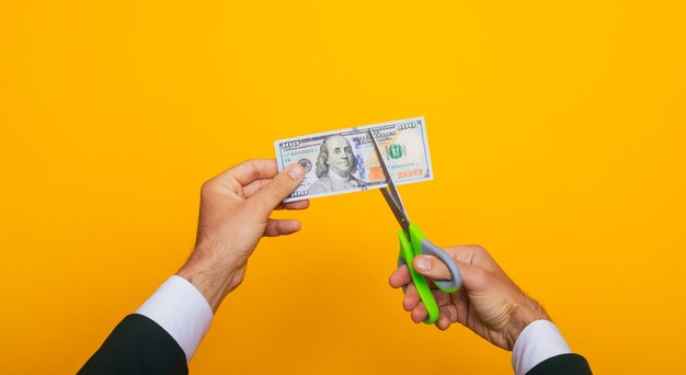 Close up photo of young human hands while cutting one hundred dollars with help of scissors