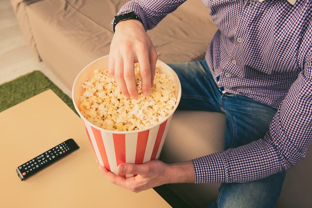 Close up photo of young man eating popcorn at home