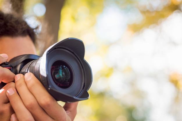 Close-up photo of young professional photographer shooting something or someone in autumn park. Fall photo session