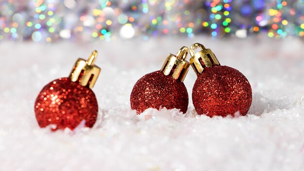 雪の中のいくつかの赤いクリスマスボールの写真をクローズアップ。背景にお祝いのボケ味。