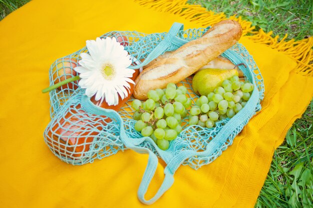 Close up of picnic bag with food, fruits and flower on the yellow cover on the green grass