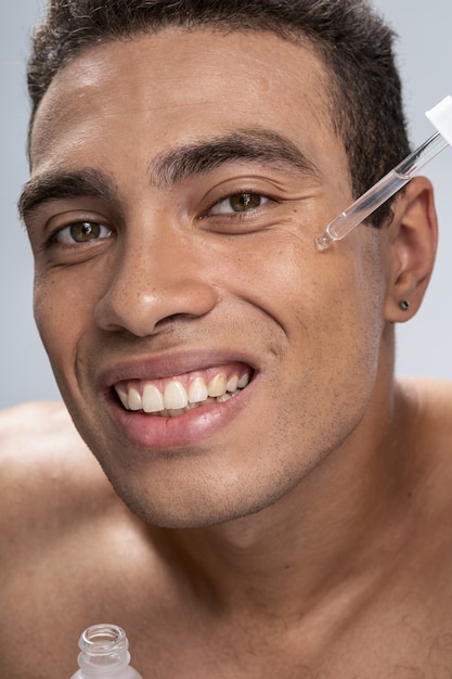 Close up picture of a cheerful young male spreading cosmetics on his face