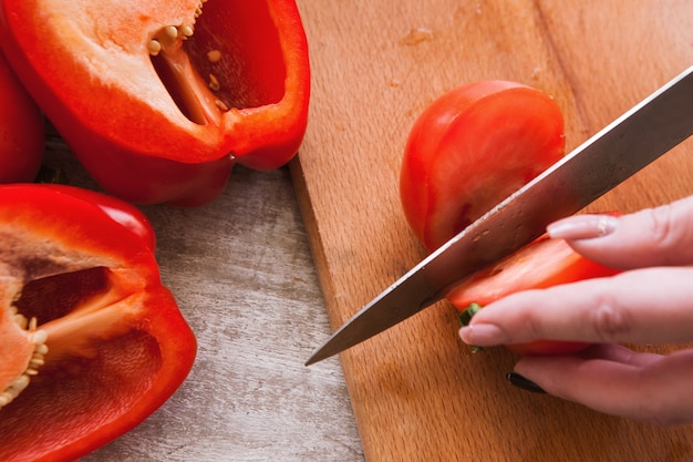 Крупным планом изображение помидоров и перца на деревянном столе, процесс приготовления салата из свежих овощей