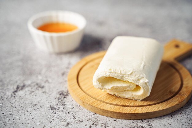 Foto immagine ravvicinata di un rotolo di burro kaymak di crema bianca lattiginosa versato con miele su un piatto di legno