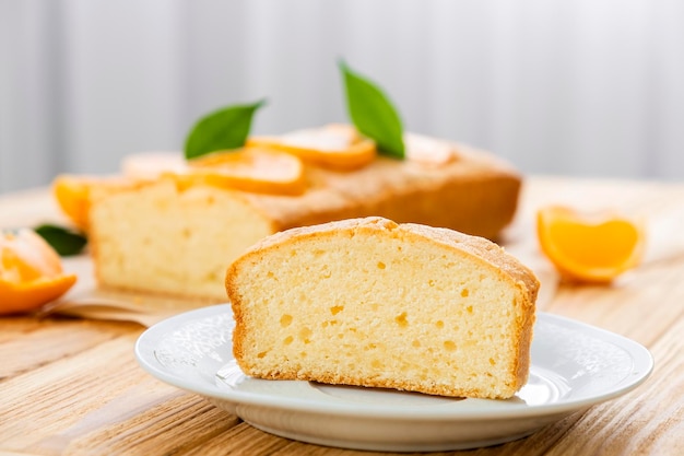 Close up piece of moist orange fruit pound cake on plate with slices of orange and whole pie on background Delicious breakfast traditional English tea time Recipe of orange pie loaf