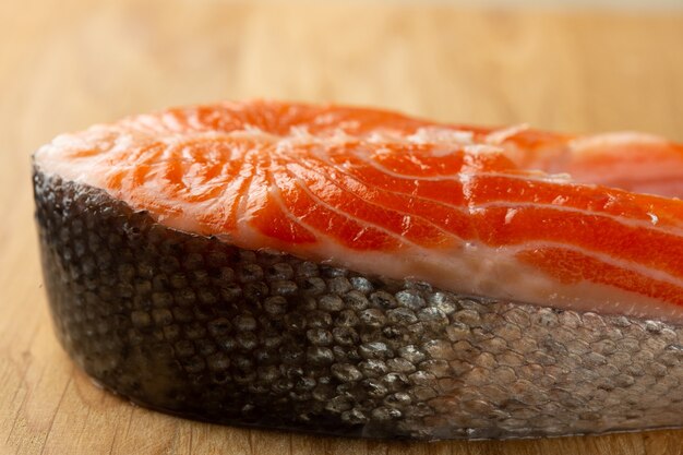 Close up of the piece of raw red salmon with clean shiny scale lying on the wooden surface