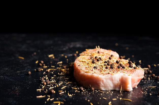 Close up on piece of raw steak meat seasoned with pepper, salt and dry rosemary on dark wooden table