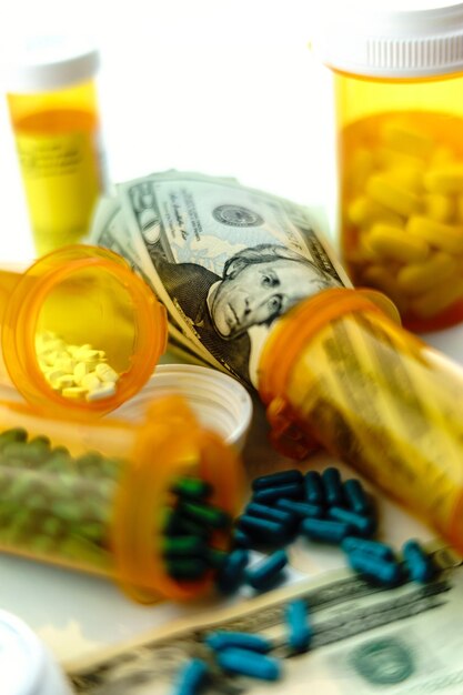 Photo close-up of pills spilling out of bottle with currency at table