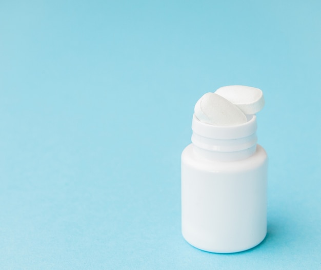 Close up pills spilling out of pill bottle on blue background. Medicine, medical insurance or pharmacy concept.