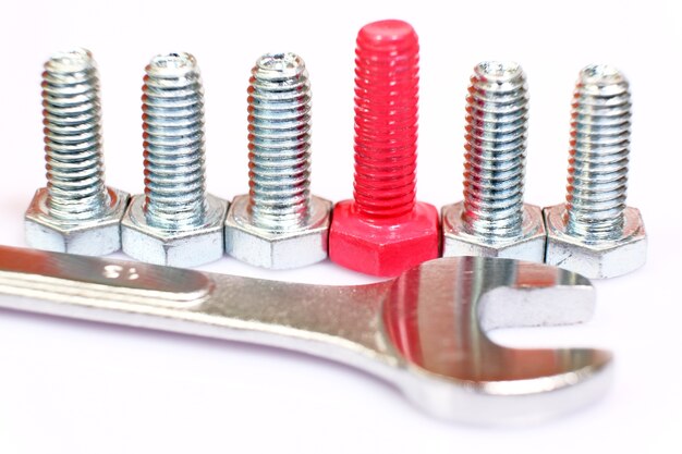 Close-up of pink bolt n a group of galvanized metallic screws and wrench. Leadership, individuality, originality concept. Stainless steel bolts isolated on white background.