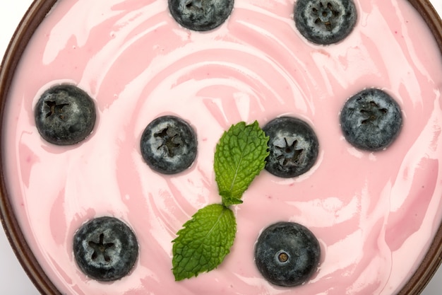 Foto chiuda sul jogurt alla frutta casalingo cremoso rosa dei mirtilli con un fondo verde fresco di struttura della foglia di menta