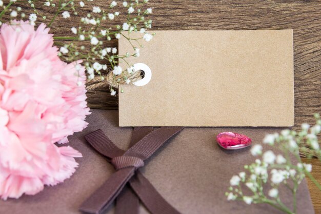 Photo close-up of pink flower by gift and empty tag on table