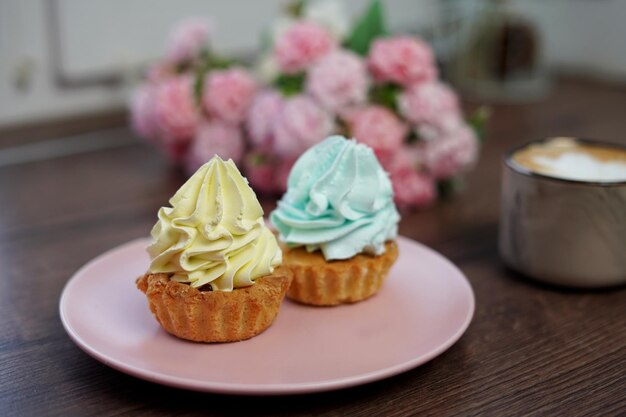 맛있는 크림 캡케이크가 있는 분홍색 접시 클로즈업이 나무 테이블에 놓여 있습니다.