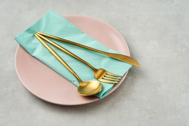 Close up of a pink plate with gold cuttlery on grey baclground