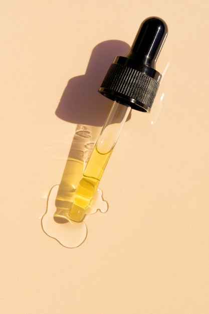 Close up of pipette with pouring liquid serum and shadows on beige background. Trendy cosmetics shot with hard shadows