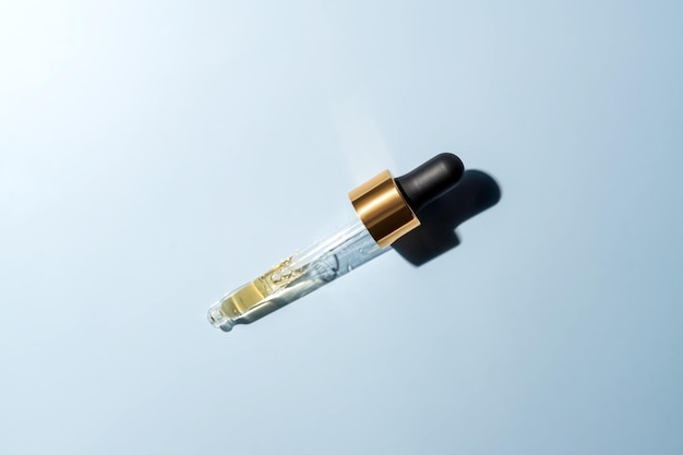 Close up of pipette with pouring liquid serum and shadows on blue background Trendy cosmetics shot with hard shadows