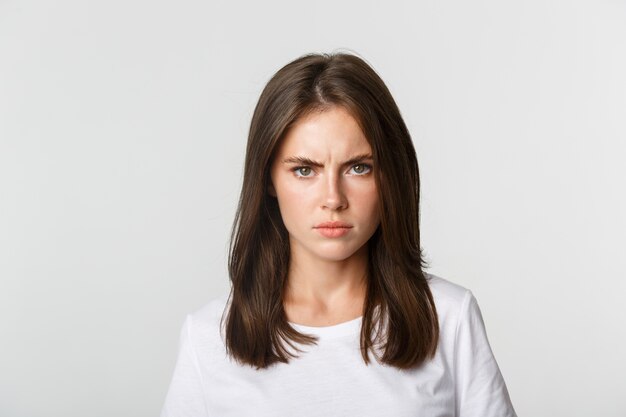 Close-up of pissed-off young girl frowning and looking angry at camera, white.